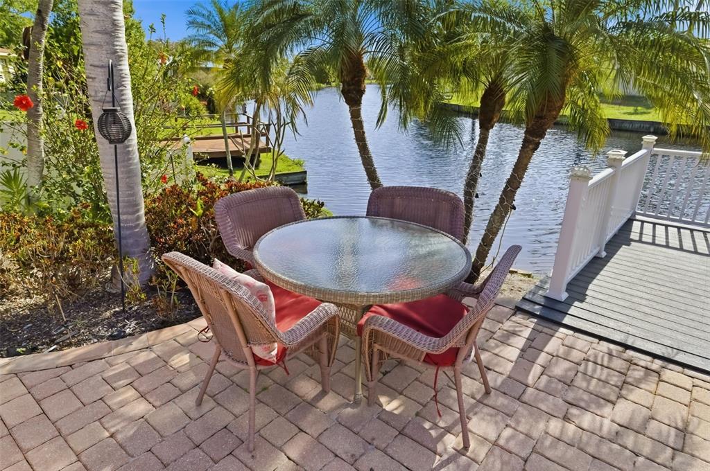 A patio with a round glass table and four wicker chairs sits beside a canal — 1207 78TH STREET NW, BRADENTON, FL