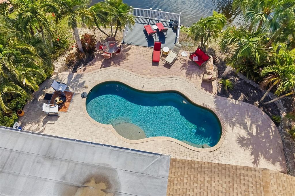An aerial view shows a kidney-shaped swimming pool, a paved patio, and a wooden dock — 1207 78TH STREET NW, BRADENTON, FL