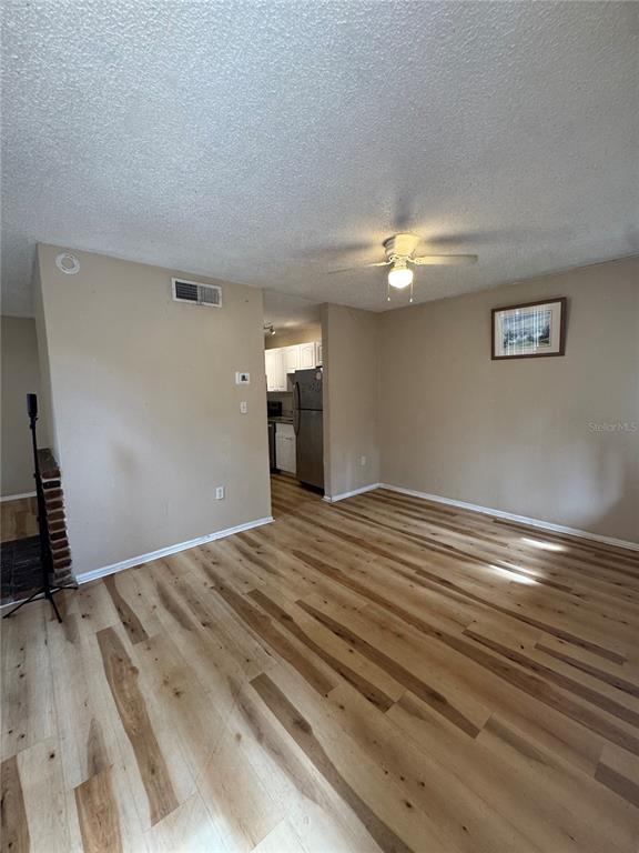 A living room with light wood-look flooring, a ceiling fan, and an adjacent kitchen — 5012 DOWNING STREET UNIT 10, ORLANDO, FL