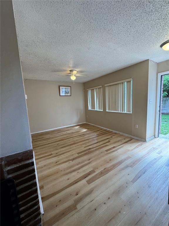 An empty living room features light wood-look flooring, beige walls, and two windows with blinds — 5012 DOWNING STREET UNIT 10, ORLANDO, FL