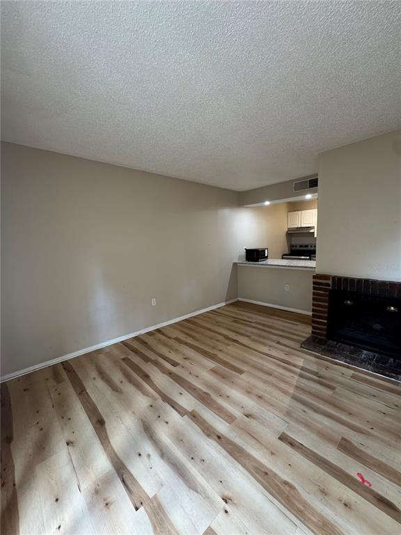 An empty living room features light wood-look flooring, beige walls, and a brick fireplace — 5012 DOWNING STREET UNIT 10, ORLANDO, FL