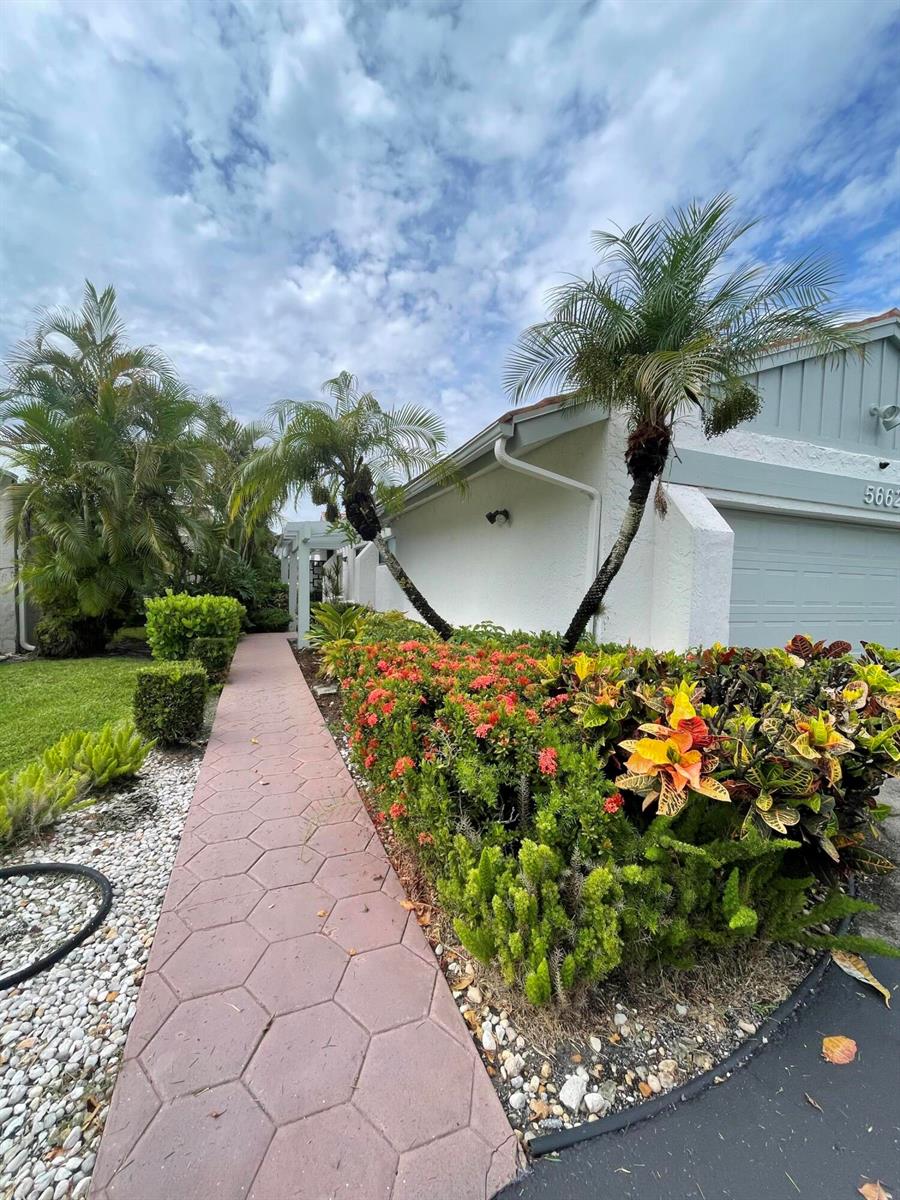 A paved walkway leads past a landscaped garden with palm trees toward a house exterior — 5662 Ainsley Court, Boynton Beach FL 33437, BOYNTON BEACH, FL