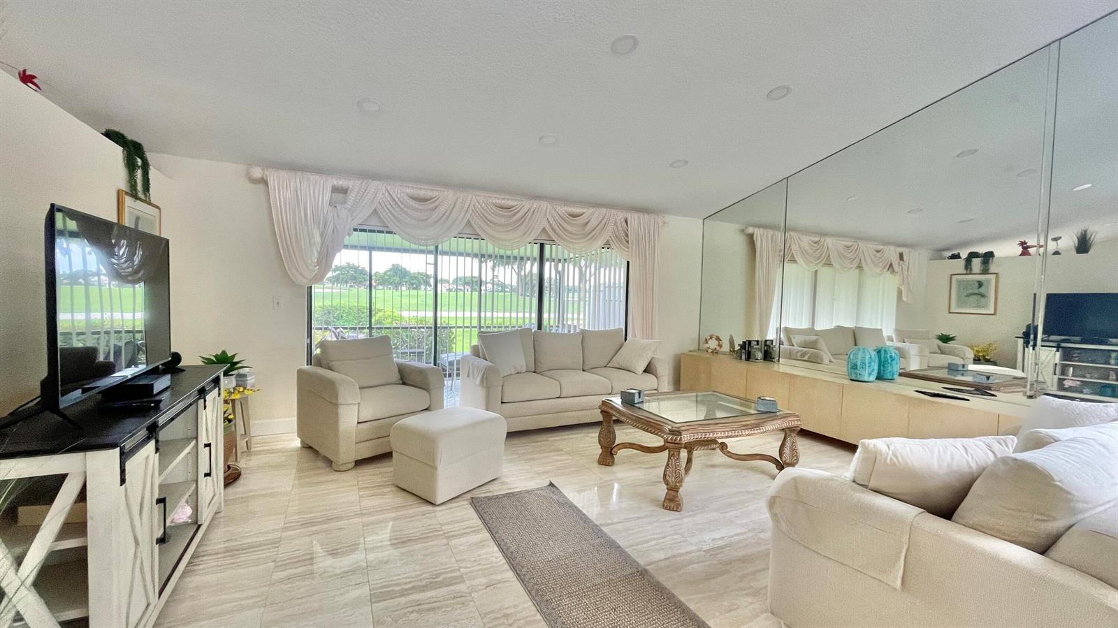 A living room features light-colored tile floors, a mirrored wall, and a view of greenery — 5662 Ainsley Court, Boynton Beach FL 33437, BOYNTON BEACH, FL