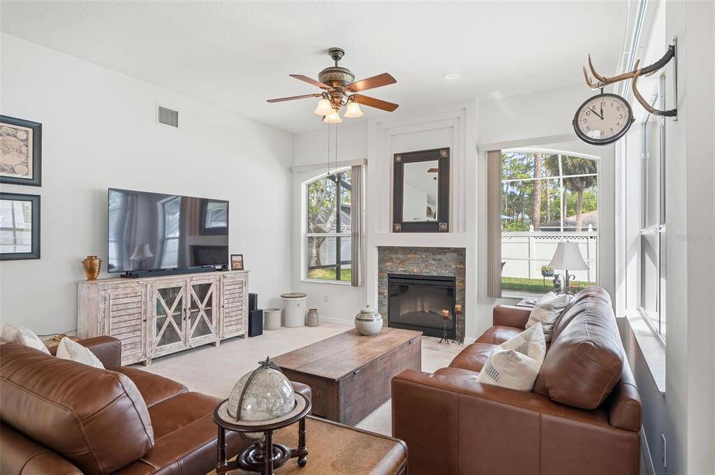 A living room features a stone fireplace, leather sofas, a ceiling fan, and large windows — 21 WOODSHIRE LANE, PALM COAST, FL