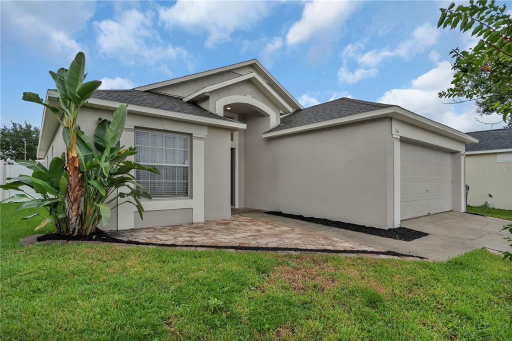 A single-story house with a beige stucco exterior, a paved walkway, and a two-car garage — 116 PIANO LANE, DAVENPORT, FL