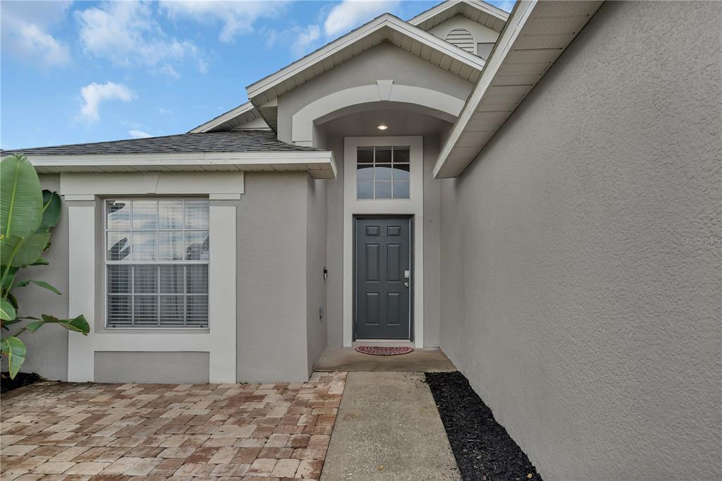 The exterior of a house features a gray front door, a window, and a walkway — 116 PIANO LANE, DAVENPORT, FL