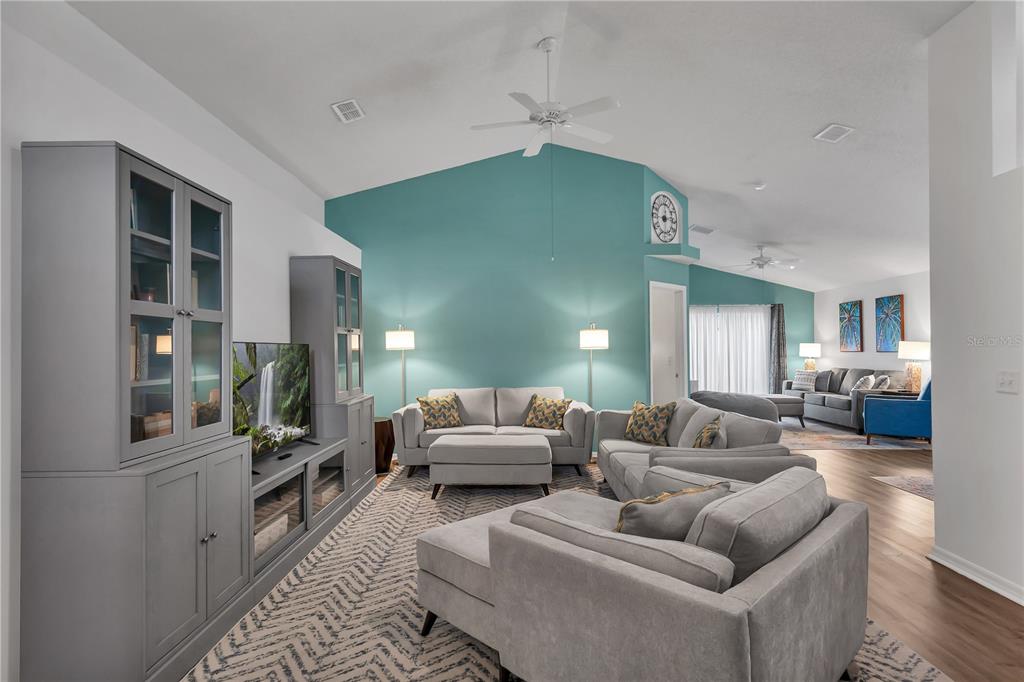 A living room features a vaulted ceiling, a teal accent wall, and gray furniture — 116 PIANO LANE, DAVENPORT, FL