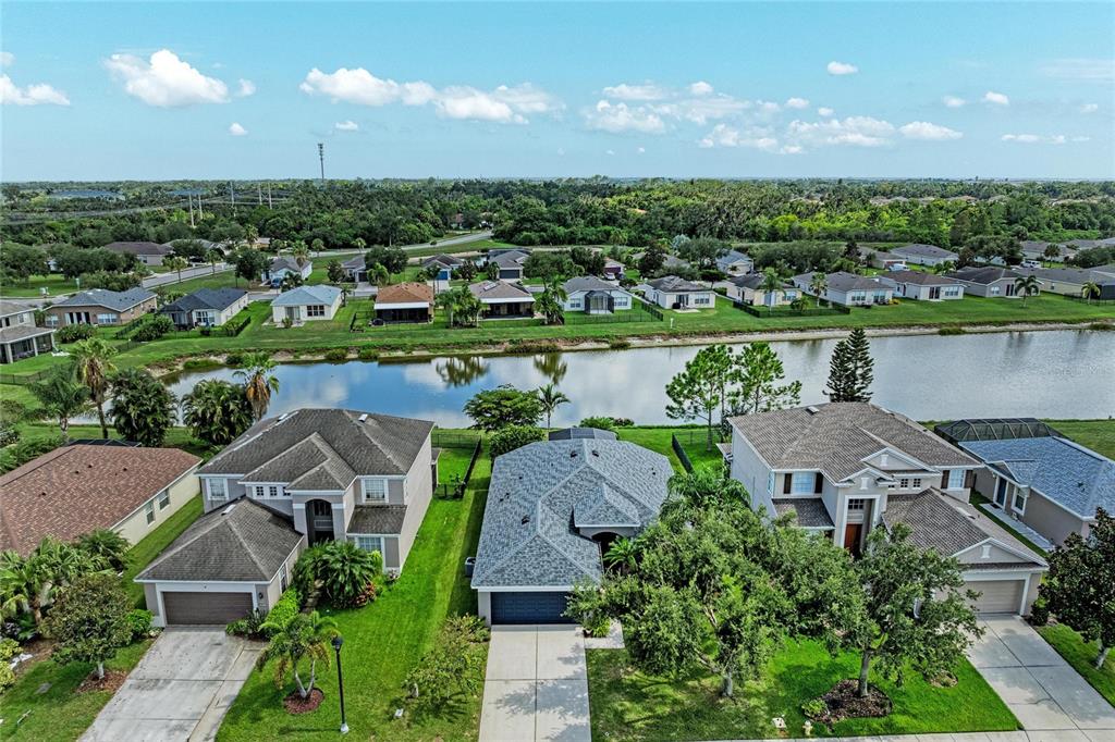 An aerial view shows three suburban houses with driveways facing a lake and neighborhood — 9947 52ND STREET E, PARRISH, FL