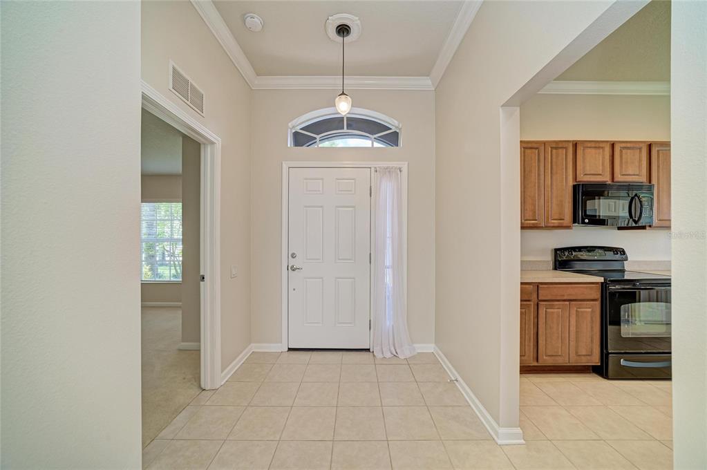 A tiled entryway leads to a white front door with a transom window and kitchen — 9947 52ND STREET E, PARRISH, FL
