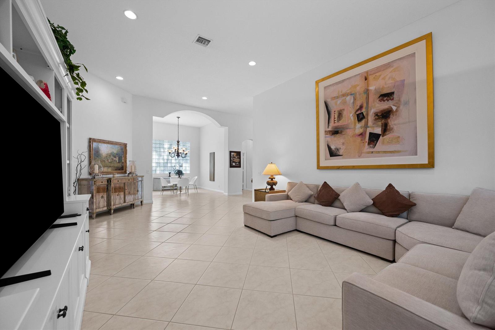 A spacious living room with tile flooring, a large sectional sofa, and a wall-mounted painting — 10689 Northgreen Drive, Lake Worth FL 33449, LAKE WORTH, FL