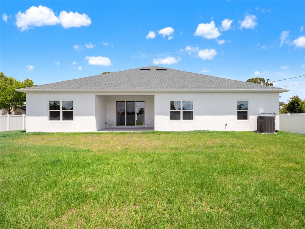 The rear exterior of a white single-story house features a covered patio and a lawn — 1406 VALERIUS STREET SE, PALM BAY, FL