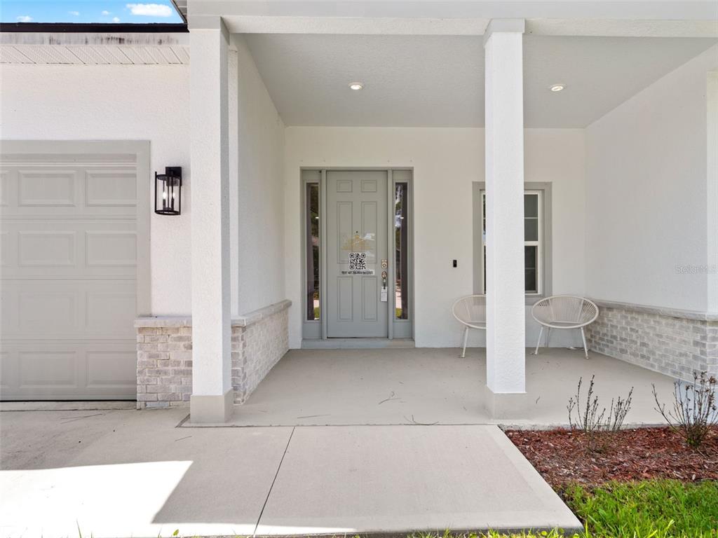 A covered front porch features a gray door, two white chairs, and stone accents — 1406 VALERIUS STREET SE, PALM BAY, FL
