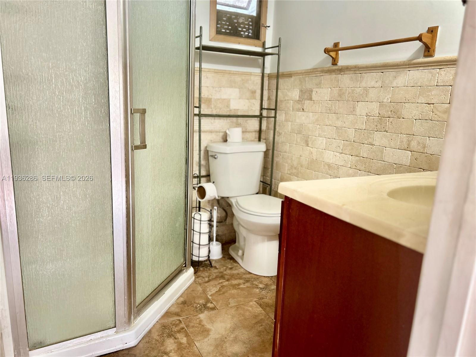A bathroom features a glass-enclosed shower, a toilet with a metal shelf, and tiled walls — 8732 SW 16th St, Davie FL 33324, DAVIE, FL