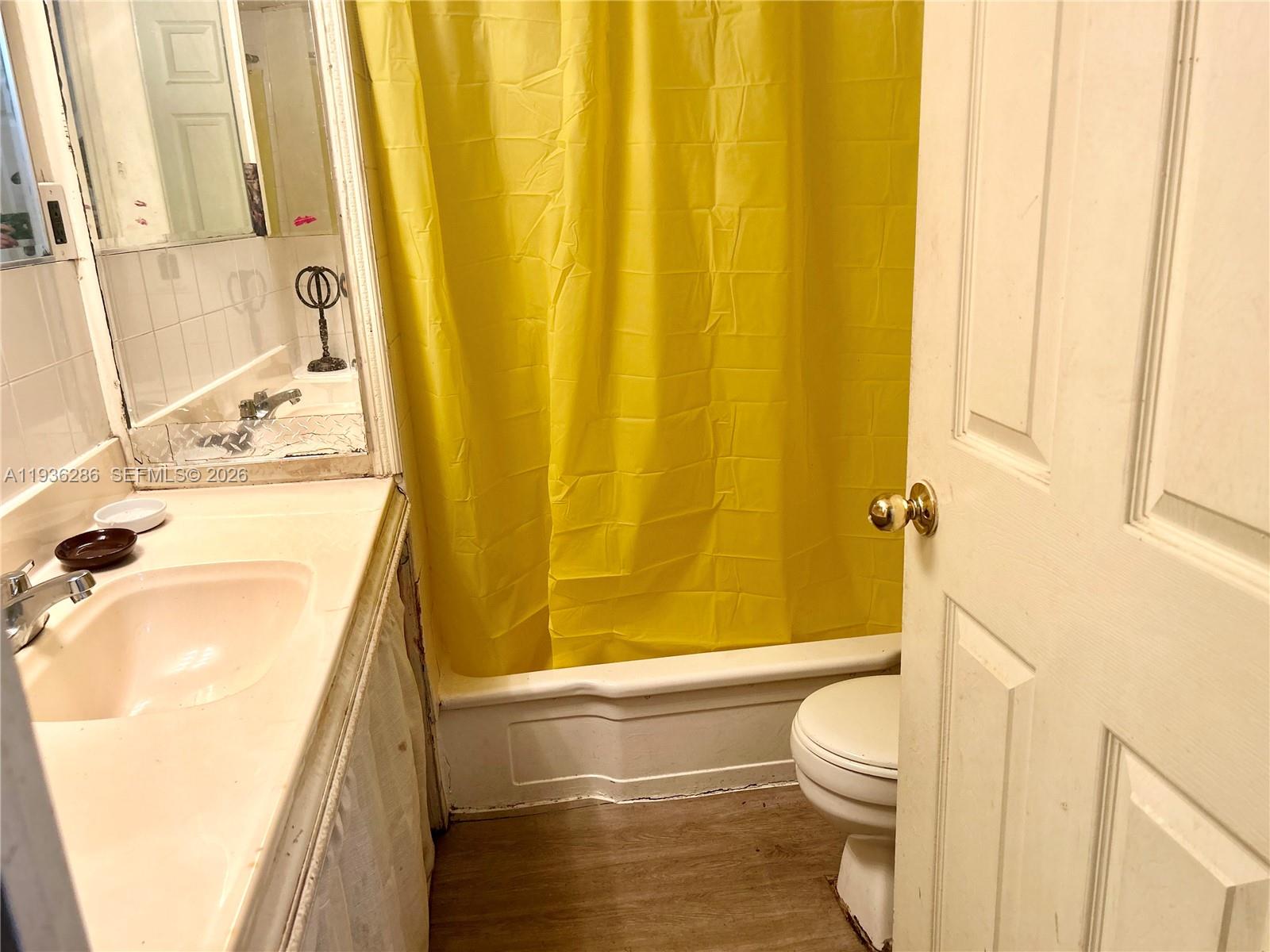 A bathroom features a vanity with a sink, a yellow shower curtain, and a toilet — 8732 SW 16th St, Davie FL 33324, DAVIE, FL