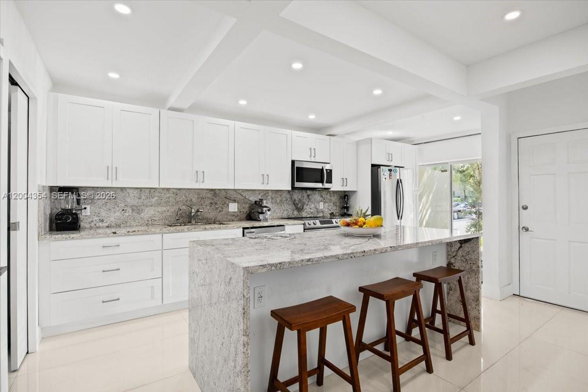 A modern kitchen features white cabinets, granite countertops, an island with stools, and recessed lighting — 19220 NE 25th Ave # 274B, Miami FL 33180, MIAMI, FL