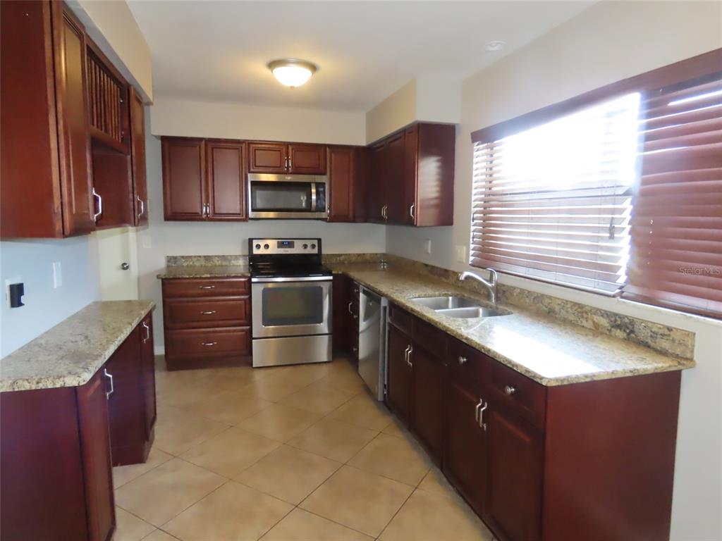 A kitchen features dark wood cabinets, granite countertops, stainless steel appliances, and tile flooring — 1743 SUNSET POINT ROAD, CLEARWATER, FL