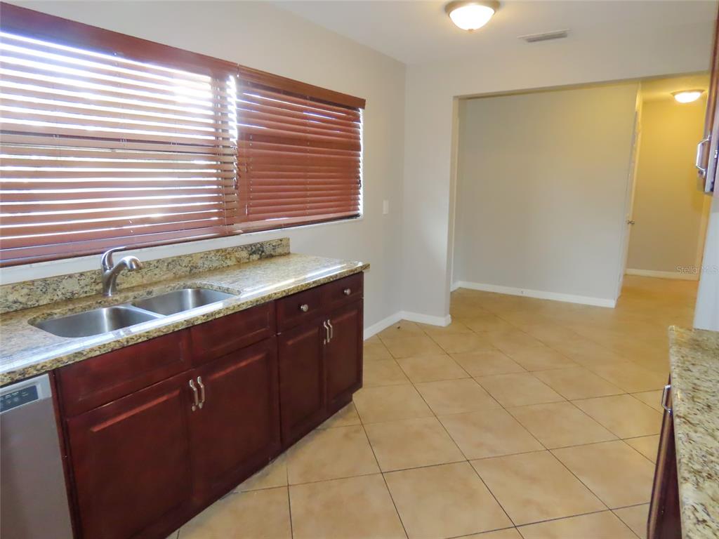A kitchen features dark wood cabinets, granite countertops, a double sink, and tile flooring — 1743 SUNSET POINT ROAD, CLEARWATER, FL