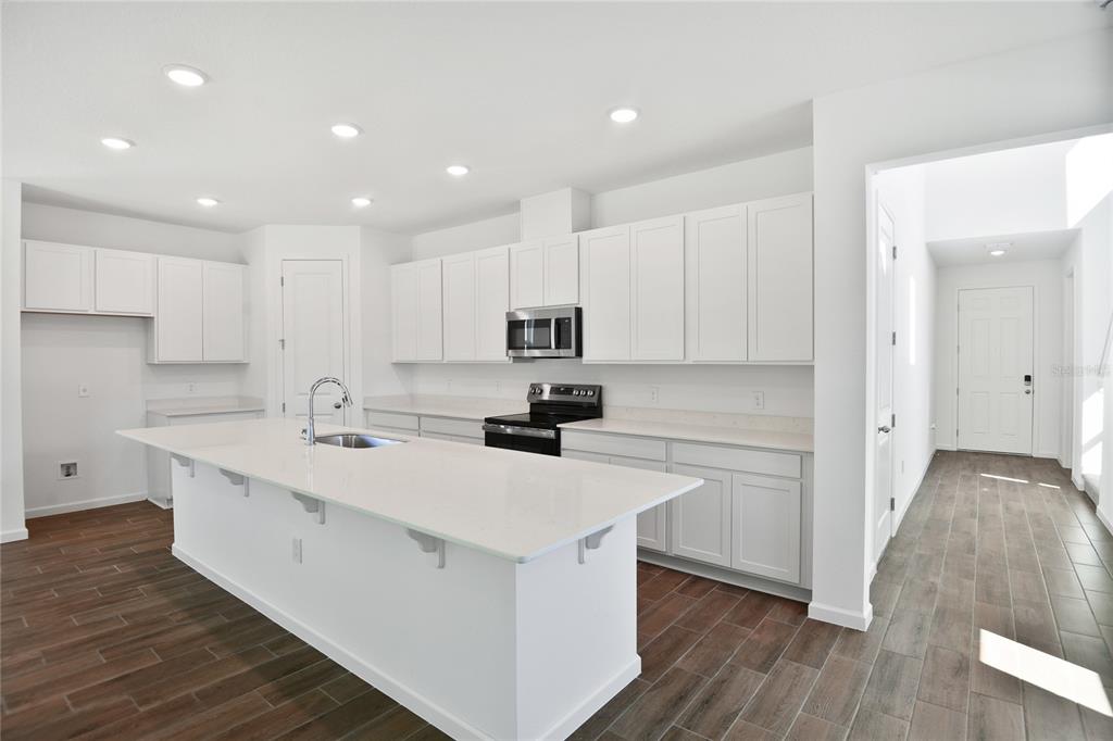 A modern kitchen features white cabinets, a large island with a sink, and wood-look flooring — 716 LAKE DELL AVENUE, DUNDEE, FL
