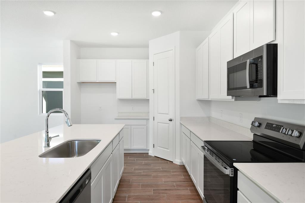 A modern kitchen features white cabinets, quartz countertops, stainless steel appliances, and wood-look tile flooring — 716 LAKE DELL AVENUE, DUNDEE, FL
