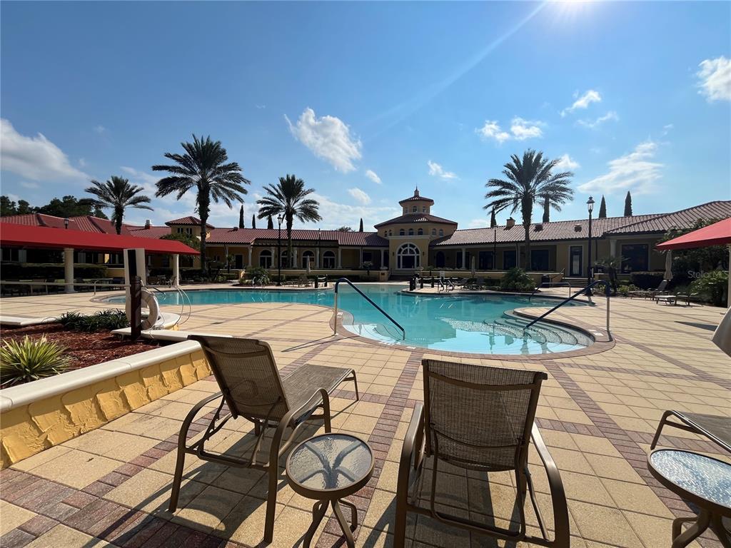 A swimming pool sits in front of a large building with palm trees and lounge chairs — 9831 DEL WEBB PARKWAY UNIT 4208, JACKSONVILLE, FL