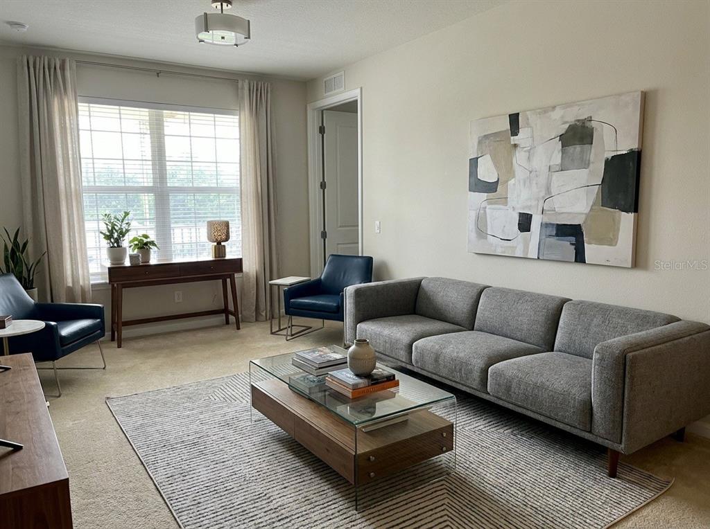 A living room features a gray sofa, a glass coffee table, and two blue armchairs — 9831 DEL WEBB PARKWAY UNIT 4208, JACKSONVILLE, FL