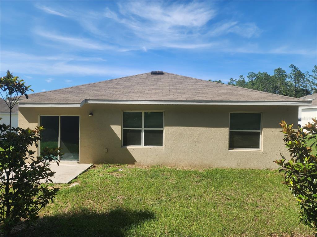 The back exterior of a single-story house features a sliding glass door and two windows — 128 HICKORY COURSE LOOP, OCALA, FL