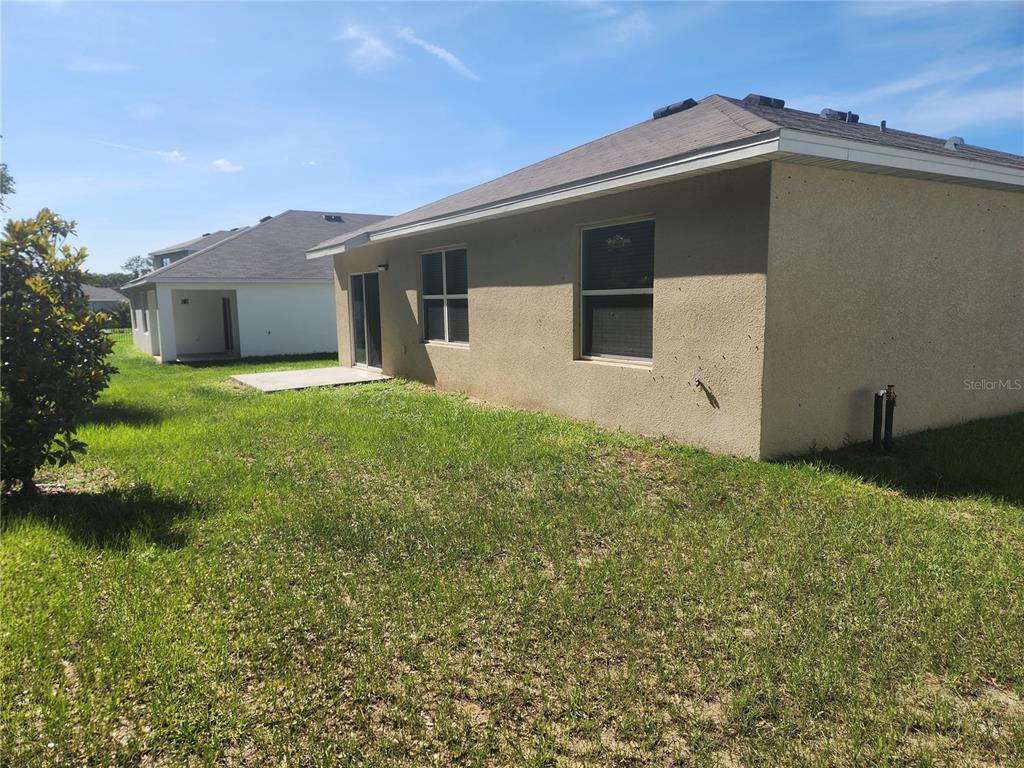 The exterior of a tan stucco house features a small concrete patio and lawn — 128 HICKORY COURSE LOOP, OCALA, FL