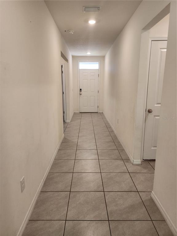 A long hallway with light-colored tile flooring leads to a white front door — 128 HICKORY COURSE LOOP, OCALA, FL
