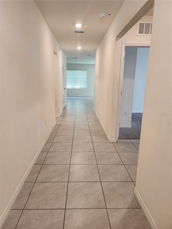 A long hallway with light-colored tile flooring leads toward a windowed room — 128 HICKORY COURSE LOOP, OCALA, FL