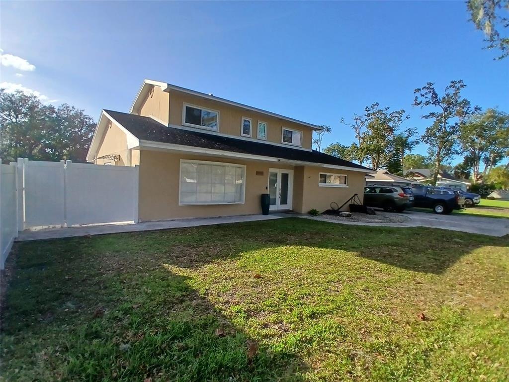 A two-story house with tan stucco siding, a white fence, and a paved driveway — 2211 NEW JERSEY ROAD, LAKELAND, FL