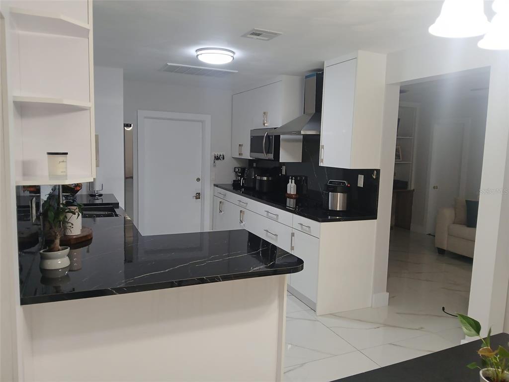 A modern kitchen features white cabinets, black marble countertops, and white tile flooring — 2211 NEW JERSEY ROAD, LAKELAND, FL