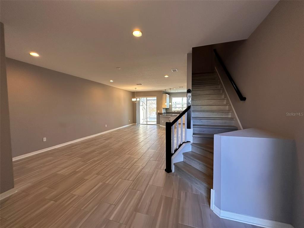 An open-concept living area features wood-look tile flooring and a staircase with black railings — 29850 SOUTHWELL LANE, WESLEY CHAPEL, FL