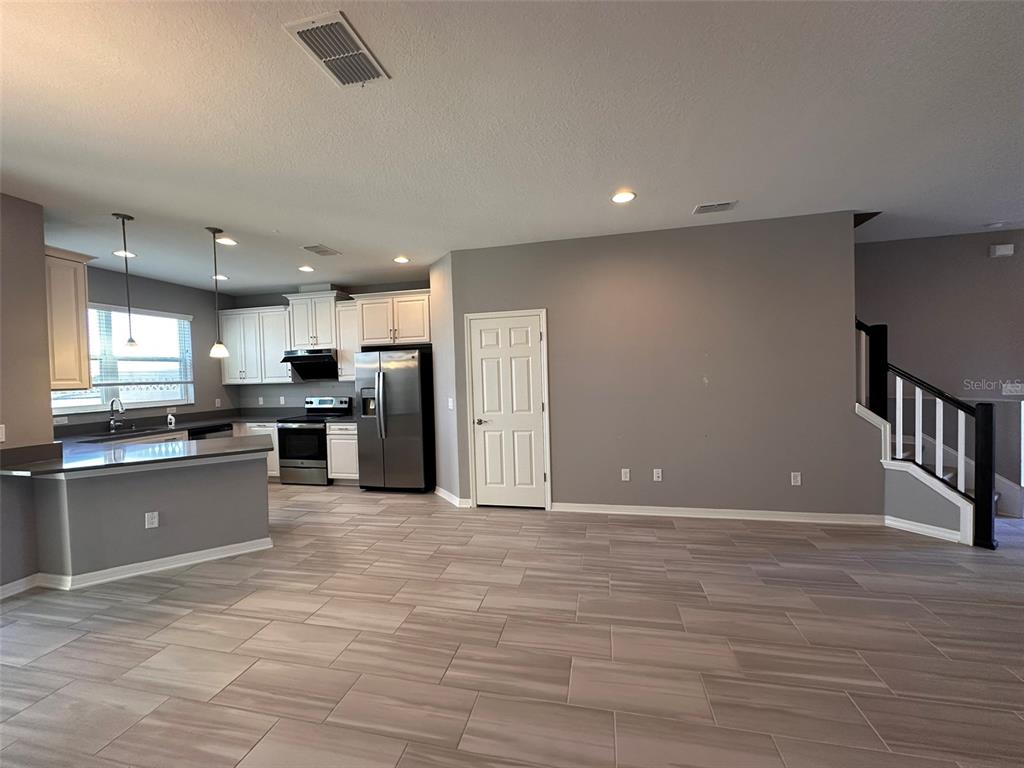 A kitchen with white cabinets and stainless steel appliances opens to a large tiled room — 29850 SOUTHWELL LANE, WESLEY CHAPEL, FL