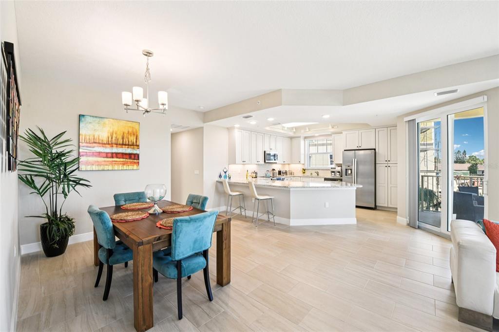 An open-concept dining area and kitchen featuring light tile floors, white cabinets, and blue chairs — 7 RIVERWALK DRIVE UNIT 307, NEW SMYRNA BEACH, FL