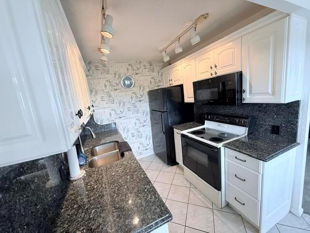 A kitchen features white cabinets, dark granite countertops, black appliances, and patterned wallpaper — 4065 Harwood E, Deerfield Beach FL 33442, DEERFIELD BEACH, FL