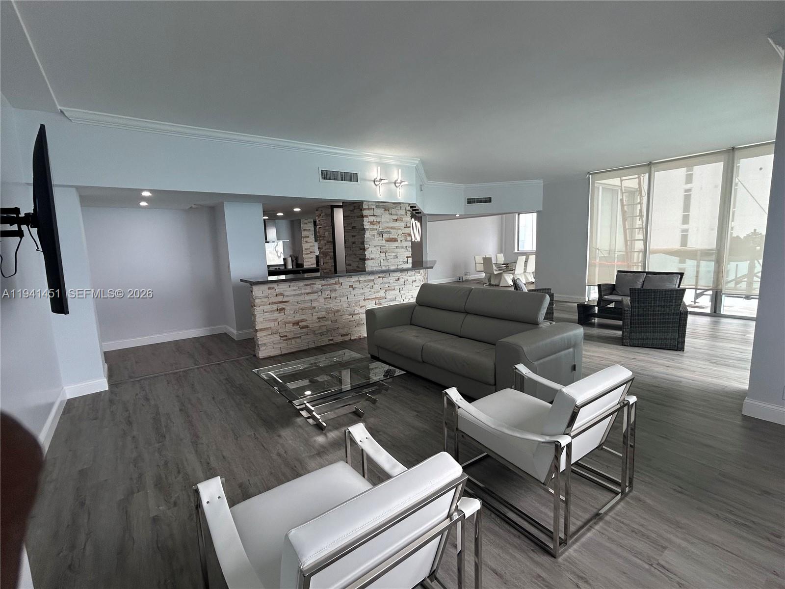 A living room features wood-look flooring, a stone-accented bar, and floor-to-ceiling windows overlooking buildings — 4001 S Ocean Dr, Hollywood FL 33019, HOLLYWOOD, FL