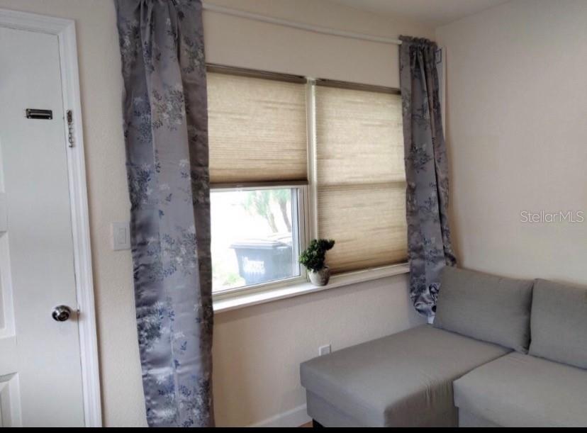 A room features a window with tan shades, patterned curtains, and a grey sectional sofa — 405 S ORION AVENUE, CLEARWATER, FL