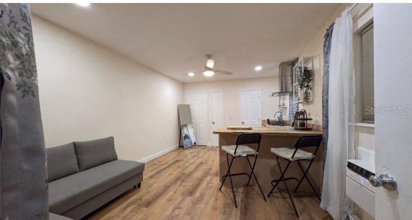 A studio apartment features wood-look flooring, a grey sofa, and a kitchen island with stools — 405 S ORION AVENUE, CLEARWATER, FL