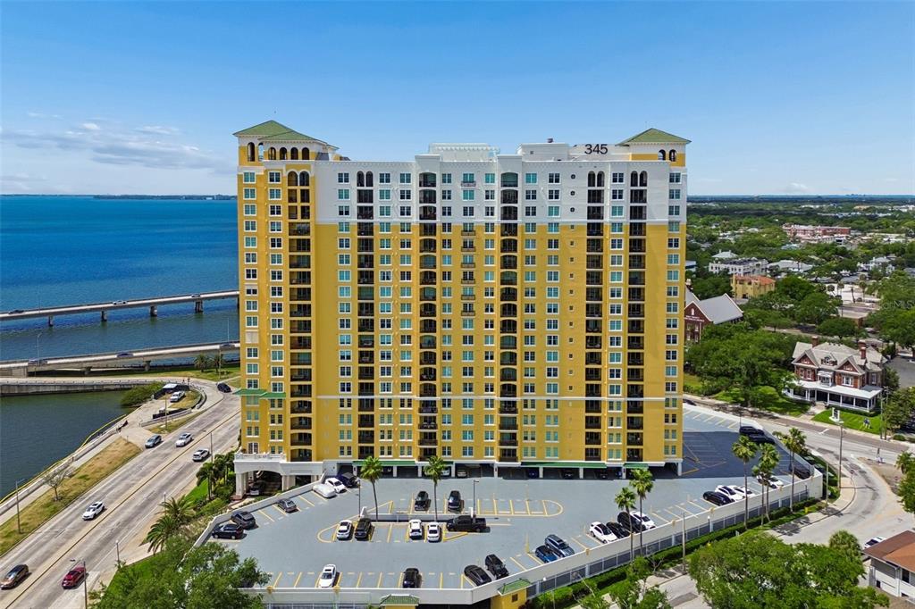 An aerial view shows a tall yellow apartment building with a parking lot and bridge — 345 BAYSHORE BOULEVARD UNIT 1206, TAMPA, FL