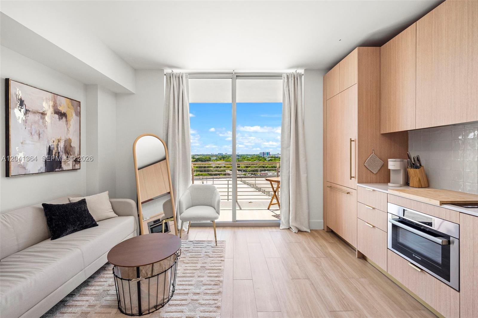 A modern studio apartment features a kitchenette, a sofa, and a balcony with outdoor views — 90 NE 32nd St # 925, Miami FL 33137, MIAMI, FL