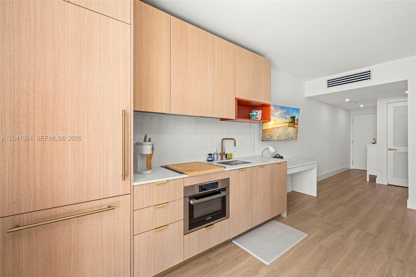 A modern kitchen features light wood cabinetry, a built-in oven, and a white tiled backsplash — 90 NE 32nd St # 925, Miami FL 33137, MIAMI, FL