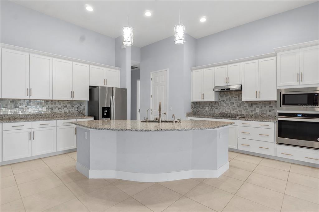 A kitchen features white cabinetry, granite countertops, a central island, and stainless steel appliances — 2320 SYMPHONY CIRCLE, ST CLOUD, FL