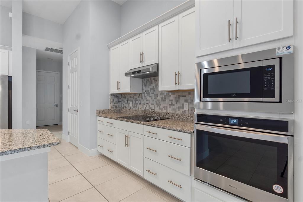 A kitchen features white cabinets, granite countertops, a tiled backsplash, and stainless steel appliances — 2320 SYMPHONY CIRCLE, ST CLOUD, FL