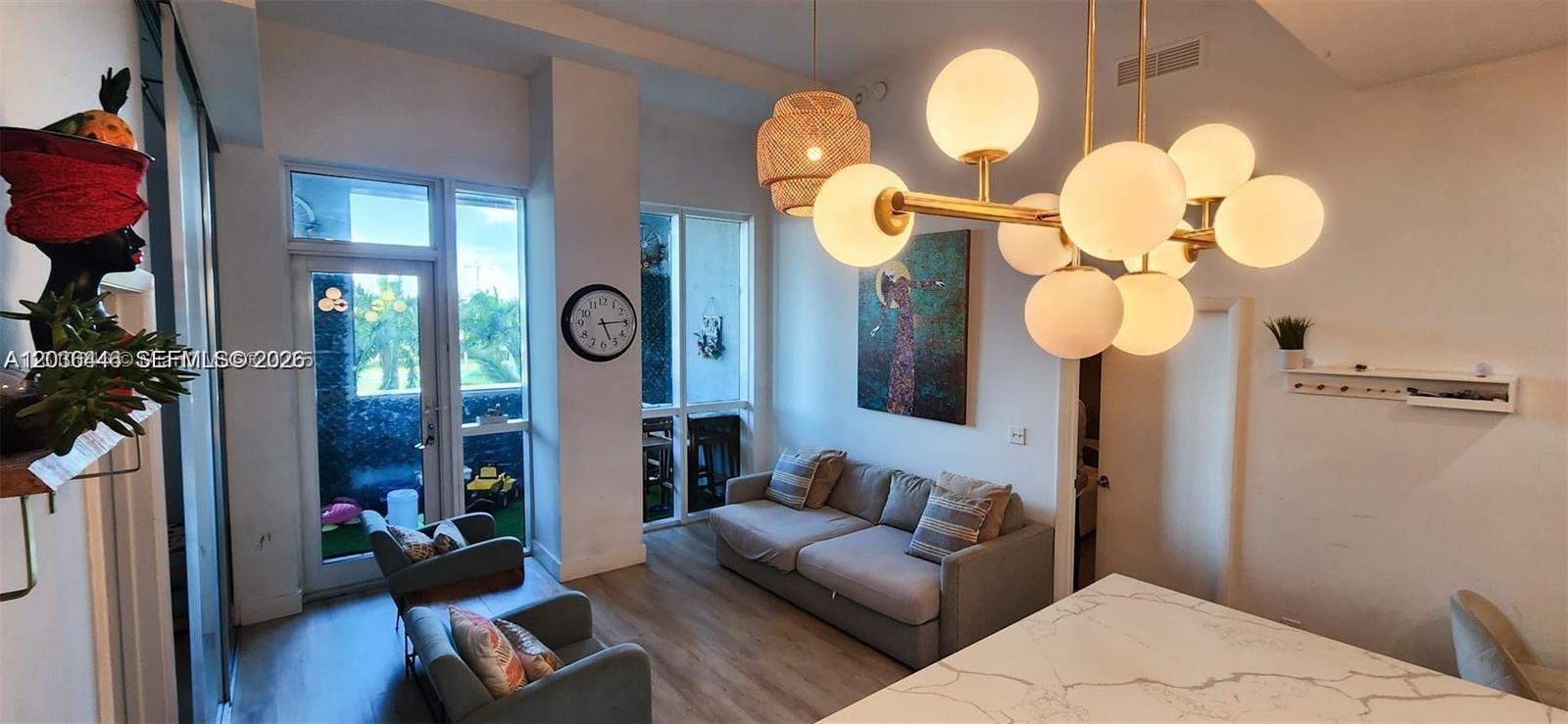 A living room features a modern chandelier, a grey sofa, two armchairs, and floor-to-ceiling windows — 244 Biscayne Blvd # 301, Miami FL 33132, MIAMI, FL