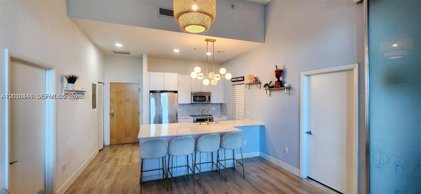 A modern kitchen features white cabinetry, a marble-topped island with four stools, and pendant lighting — 244 Biscayne Blvd # 301, Miami FL 33132, MIAMI, FL