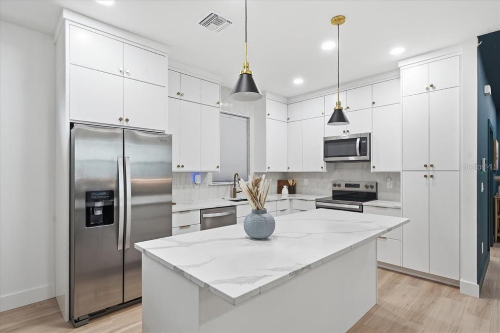A modern kitchen features white cabinetry, stainless steel appliances, and a marble-topped center island — 2601 E 24TH AVENUE, TAMPA, FL