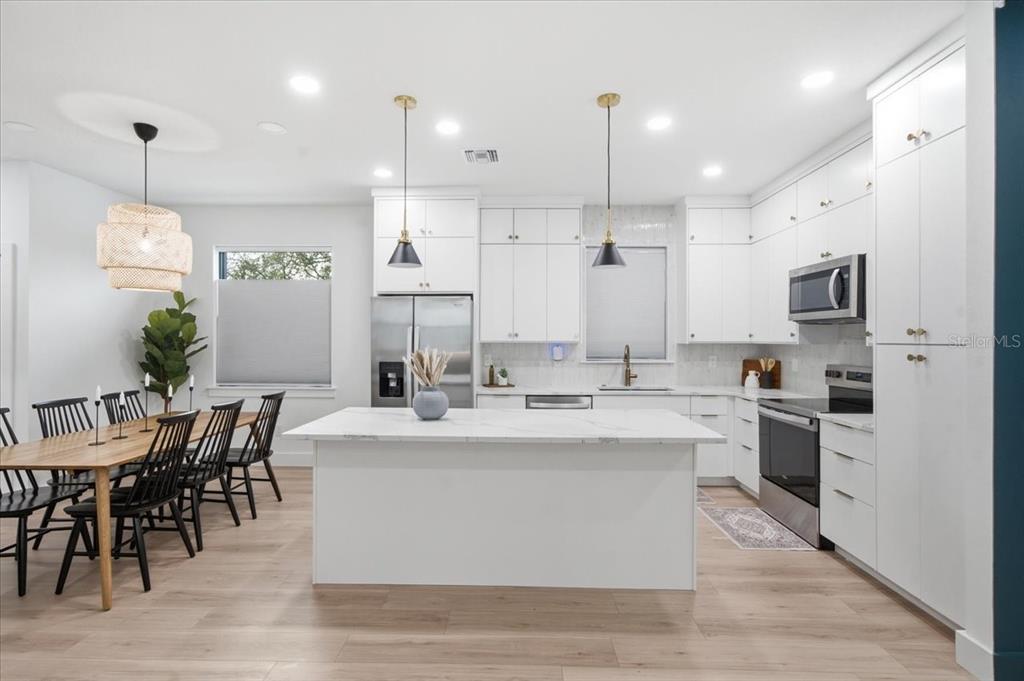 A modern kitchen features white cabinetry, a marble-topped island, and an adjacent dining area — 2601 E 24TH AVENUE, TAMPA, FL