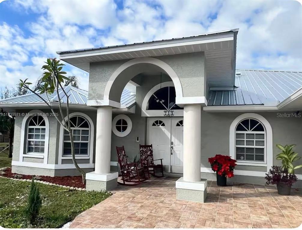 A single-story house exterior features a covered entryway with two columns and a metal roof — 713 5TH AVENUE, LEHIGH ACRES, FL