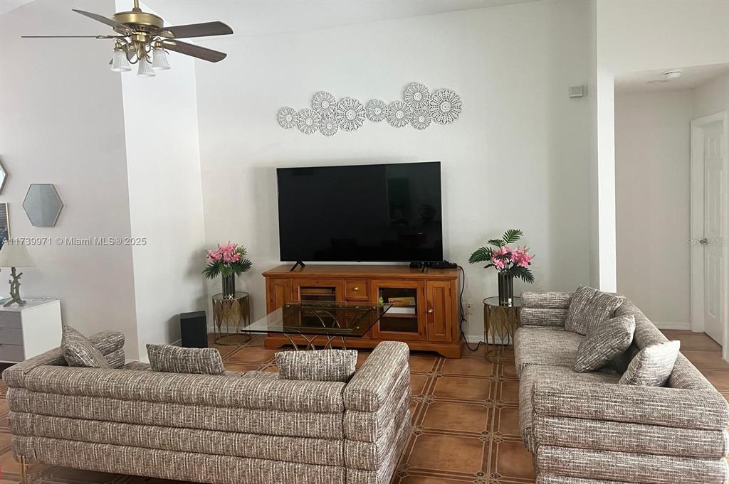 A living room features a television on a wooden stand, two sofas, and tiled flooring — 713 5TH AVENUE, LEHIGH ACRES, FL