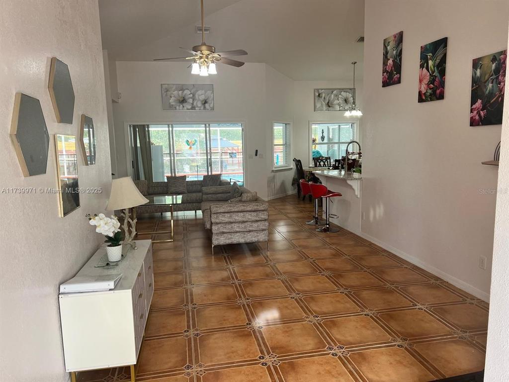 An open-concept living and dining area features tiled floors, a ceiling fan, and bar seating — 713 5TH AVENUE, LEHIGH ACRES, FL